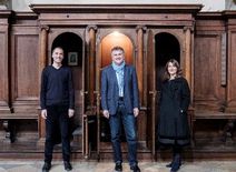 Drei Personen vor einem Beichtstuhl